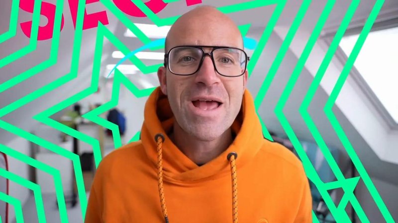 Close-up shot of Daniel Walter Scott positioned in front of vibrant, concentric neon green star outlines and pink background shapes.