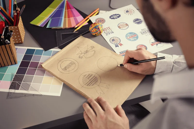 Man sketching logos with swatches of colour on desk.