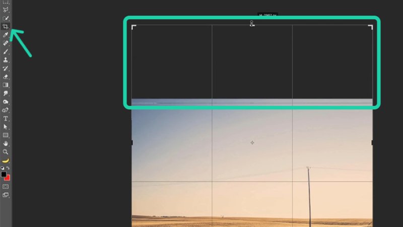 Highlighted crop tool in toolbar and cropping area grid over countryside image in adobe photoshop