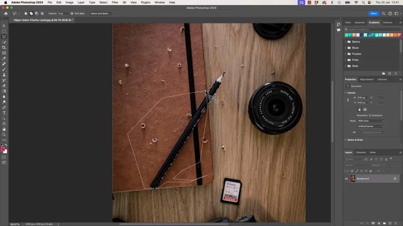 Close-up of the wooden desk in Adobe Photoshop 2024 with animated marching ants outlining the brown leather journal and black pencil, as the polygonal lasso cursor draws straight selection lines along the edge