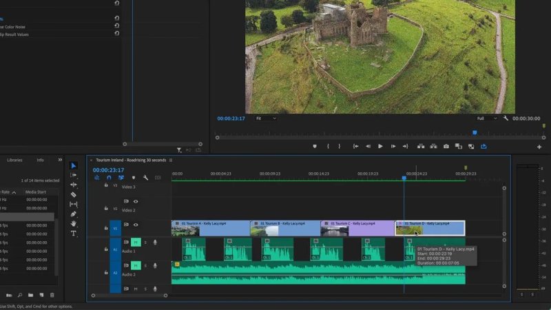 Premiere Pro interface with the playhead parked at twenty-three seconds over an active clip labeled Tourism D, displaying an aerial drone view of green hills and ancient stone ruins in the Program Monitor.